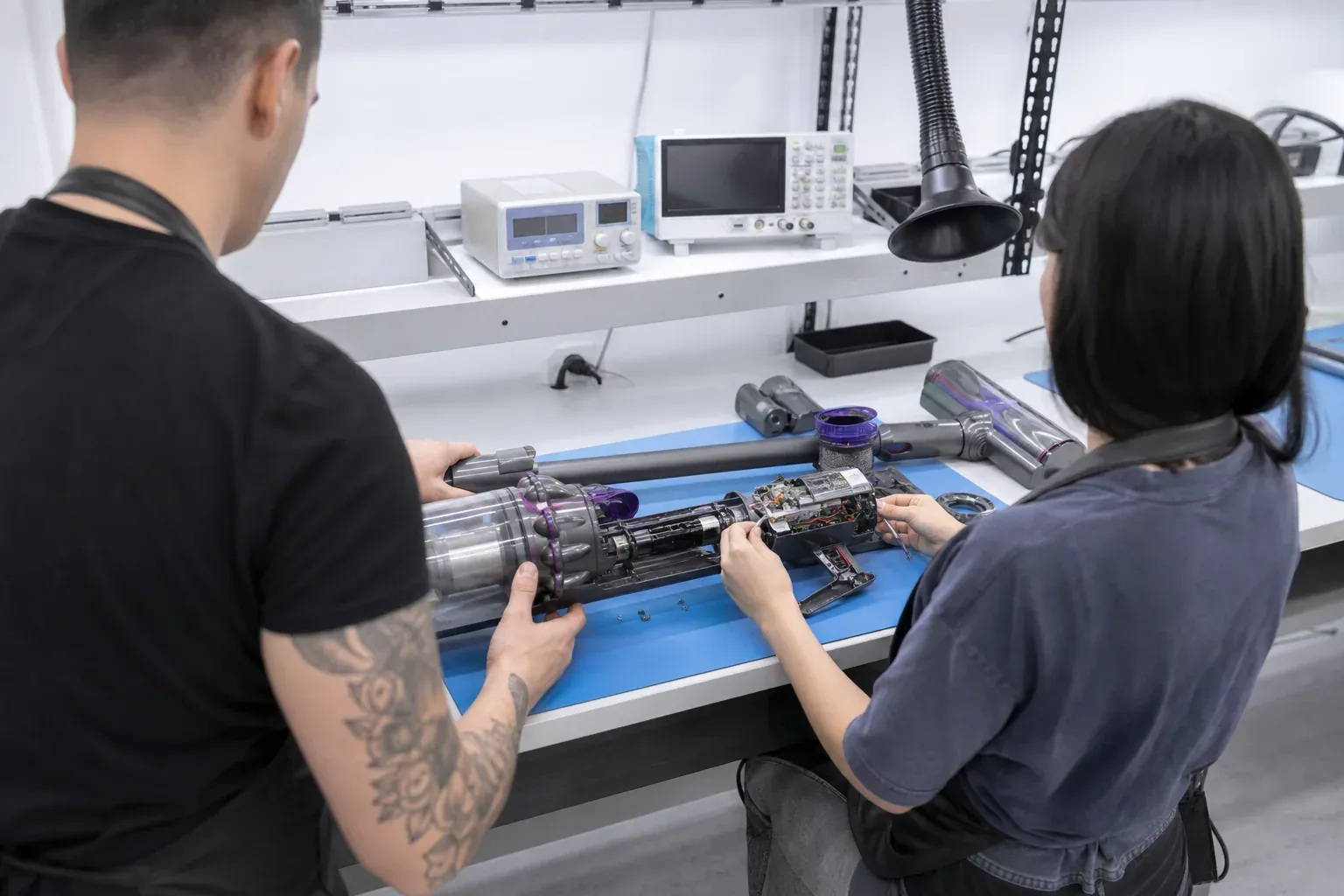 Dos técnicos del taller abriendo juntos una unidad de aspiradora sin cable en el banco compartido