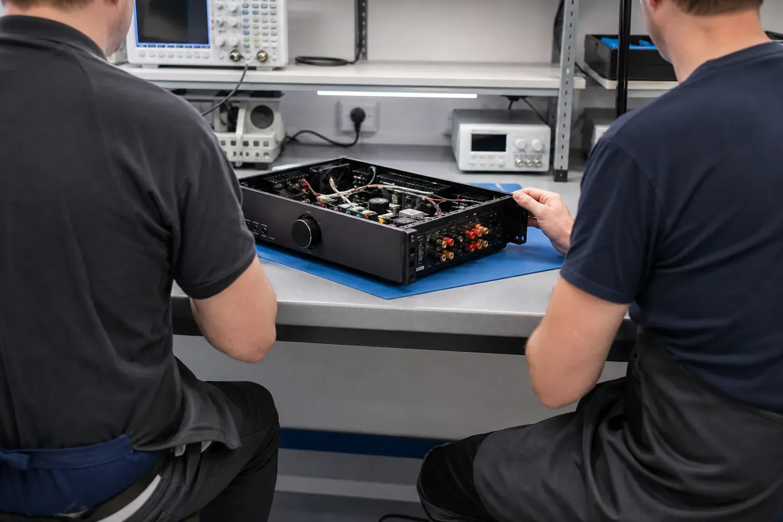 Dos técnicos del taller abriendo juntos una unidad de HI-FI y amplificador en el banco compartido